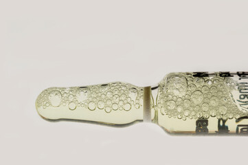 Transparent ampoule with yellow liquid and bubbles on white background. Glass medical ampoule with medicine. Close-up of bubbles in medicine ampoule.