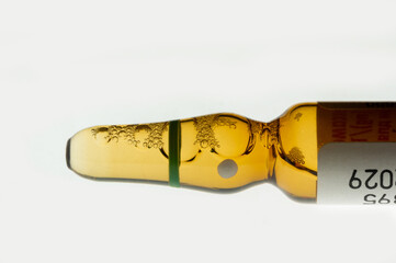 Golden medical ampoule with bubbles on white background. Close-up of glass ampoule with liquid and foam. Medical container with yellow liquid.