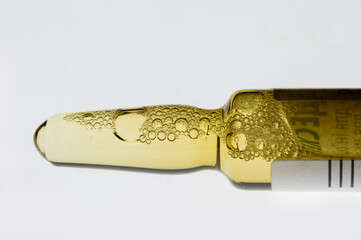 Golden medical ampoule with bubbles on white background. Close-up of glass ampoule with liquid and foam. Medical container with yellow liquid.