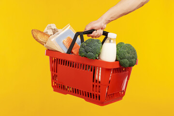 Man holding shopping basket with different products on yellow background, closeup