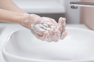Woman washing hands at sink in bathroom, closeup