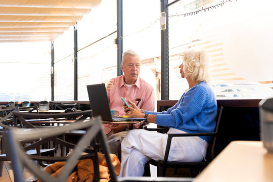 Senior russian couple using laptop and smartphone in outdoor cafe
