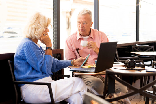 Senior russian couple enjoying free time at outdoor cafe, using technology