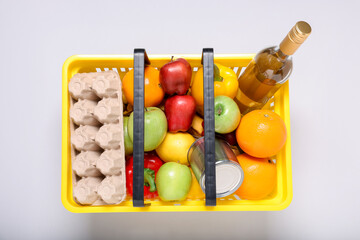 Plastic shopping basket full of products on light background, top view