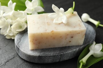 Bar of soap and jasmine flowers on black table, closeup