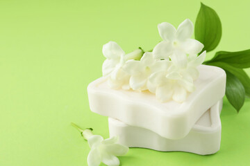 Bars of soap and jasmine flowers on light green background, closeup. Space for text