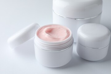 Jars of moisturizing body cream on white background, closeup