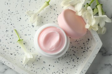 Jar of moisturizing body cream and flowers on white marble table, flat lay