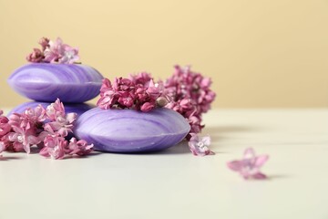 Soap bars and lilac flowers on white table against beige background, closeup. Space for text