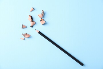 Sharp graphite pencil and shavings on light blue background, top view