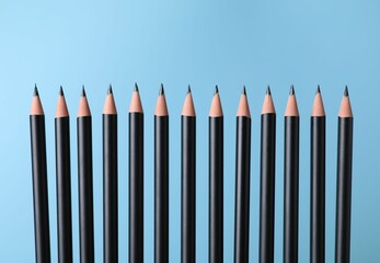 Many sharp graphite pencils on light blue background, closeup
