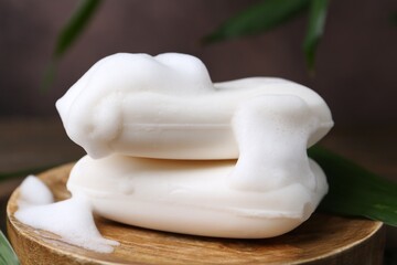Soap bars with foam on wooden table, closeup
