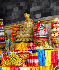 A richly decorated Buddhist altar featuring a golden Buddha statue surrounded by fruit towers,...