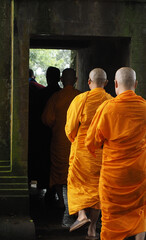 A group of Buddhist monks in orange robes walking through an ancient stone temple entrance