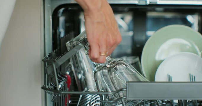 Girl loading dirty plates and glass in dishwasher. Puts dirty dishes in dishwasher machine. Housewife uses modern appliance to keep clean kitchen.