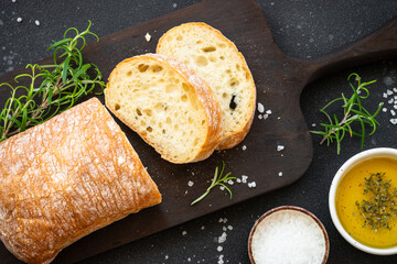 Ciabatta bread on wooden board with olive oil, olives and herbs.