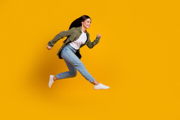 Young energetic woman jumping on a vibrant yellow background showcasing casual fashion and positivity