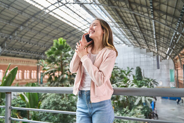 Fototapeta premium Young woman talking on smartphone and gesturing in station