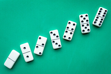 The game of dominoes is a table game involving rectangular pieces with dots that represent numbers. The objective is to match tiles with matching numbers. Photo with green background.