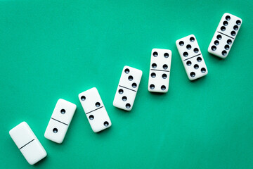 The game of dominoes is a table game involving rectangular pieces with dots that represent numbers. The objective is to match tiles with matching numbers. Photo with green background.