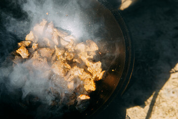 Pieces of meat frying in oil in a large cast iron cauldron with steam. Cooking outdoor in a big pot for holiday.