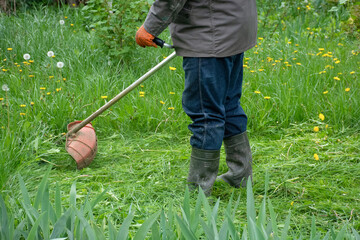 Man in the garden mowing tall grass with hand mower, garden care. High quality photo