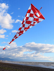 Fototapeta premium Red and White Checkered Kite Soaring High Above Beach