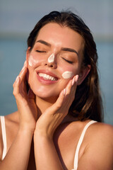 Beautiful Woman Face Portrait. Beauty Skin Care Concept. Young Woman Applying Lotion on Face. A Girl Uses Moisturizer Sunscreen. Solar Cream. Sun protection. Sunblock