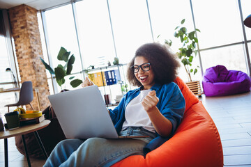 Young professional woman in a casual workspace celebrating success while working on a laptop in a...