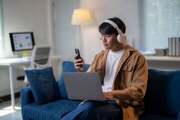 A man is sitting on a couch with a laptop and a cell phone in his hands