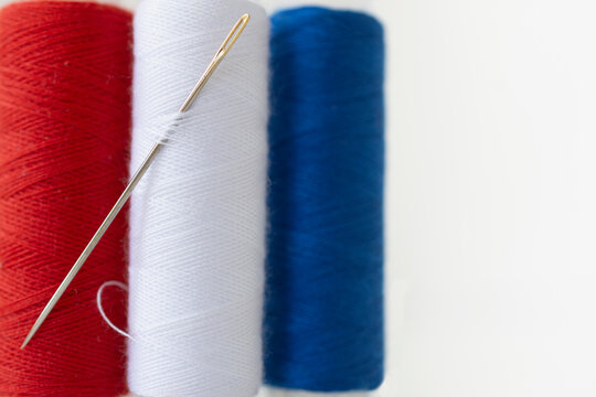 Studio shot of needle and spools of red, white and blue thread