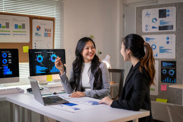 Two women are sitting at a desk with a lot of graphs
