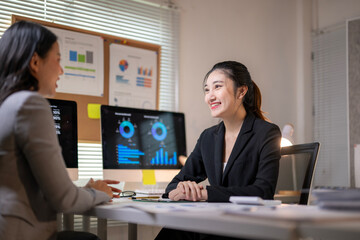 Two women are sitting at a desk with a board behind them