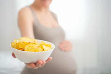 Expecting mother holding plate of chips while gently touching her belly. Realistic moment of...
