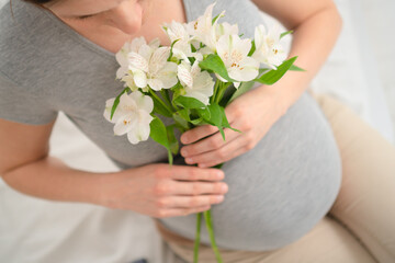 Expecting mother cradling white flowers while lovingly touching her baby bump. Pregnant woman