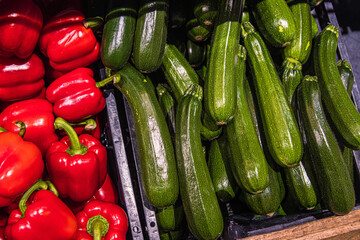 Red bell peppers and zucchinis on grocery store shelf. Fresh paprika and green zucchinis displayed in a produce aisle.