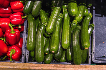 Red bell peppers and zucchinis on grocery store shelf. Fresh paprika and green zucchinis displayed in a produce aisle.