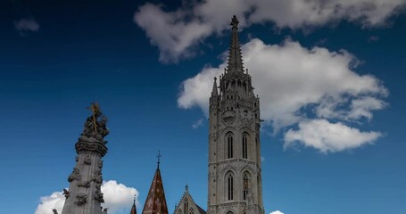 Budapest, Hungary - April 19, 2025: People walking near Matthias Church and Holy Trinity Statue: Buda’s Sacred Duo. Timelapse, zoom out transition.