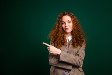 Confident young businesswoman in formalwear pointing at copy space against an emerald green...