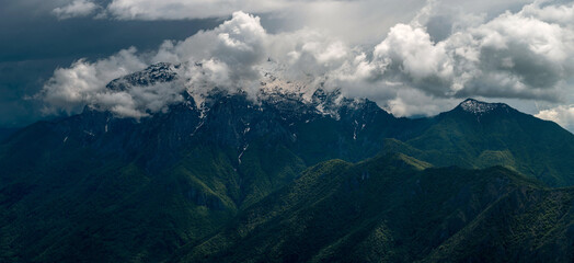 Expansive panorama showcasing Grigna Settentrionale and Pizzo della Pieve, with dramatic light illuminating the vibrant green slopes below, contrasted against high-contrast clouds above. Lombardy