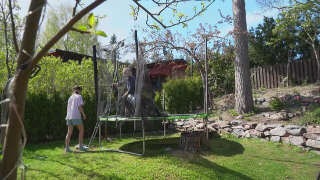 Family assembling trampoline in backyard on sunny spring day. Father and daughter setting up frame together. Outdoor activity, teamwork, home garden scene.