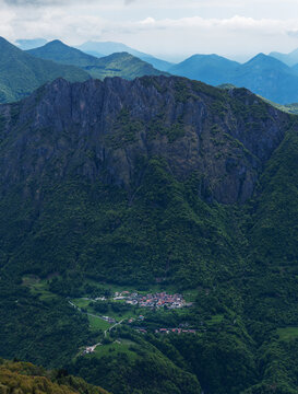 Idyllic vertical composition showcasing the charming village of Parlasco, compactly nestled amidst the lush green slopes of Valsassina, under the watchful gaze of the Prealpi Lombarde. Italy.