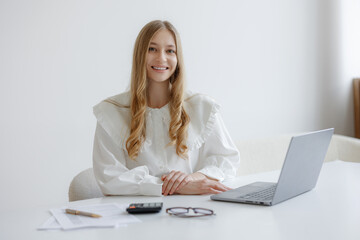 Young woman in a white blouse working on a laptop at a desk with documents and calculator in a...