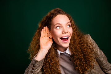 Excited young woman with curly hair gesturing enthusiasm against a vibrant emerald background,...