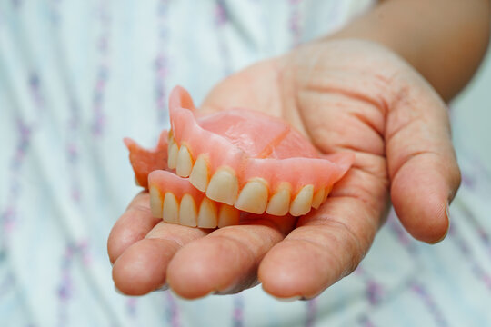Asian senior woman patient holding teeth denture in her hand for chew food.
