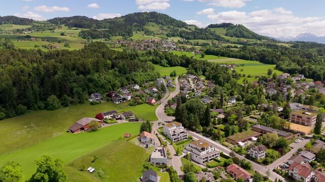 Drone flight over swiss city of Hinwill with luxury apartment houses in idyllic mountains of Switzerland. Aerial forward wide shot. Green forest landscape and hills in distance. Modern buildings.