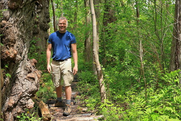 Middle-aged hiker in a blue shirt smiling while standing next to an interesting tree in the woods