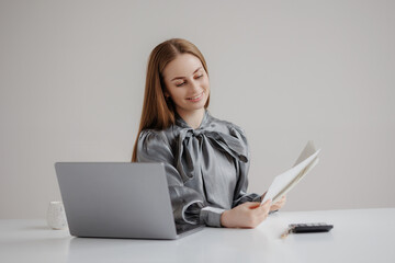 Professional woman reviewing documents at a sleek office desk during daytime with a laptop and calculator nearby