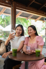 Mom and daughter laughing and smiling in a cafe taking selfie with mobile phone