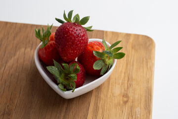 Ripe strawberries on a heart-shaped plate on a light background. Healthy food.
